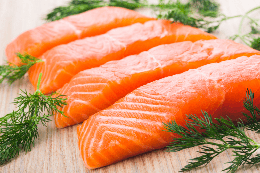 Fresh salmon fillets with dill on a wooden board, displaying the orange-pink hue and delicate texture of the fish.